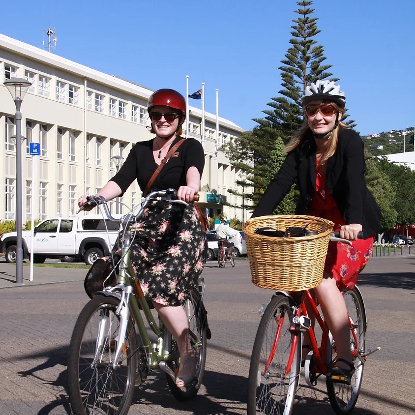 Two women smile as they bike along a footpath